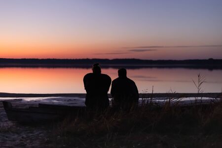 Couple sitting on the lake shore watching sunsetの写真素材