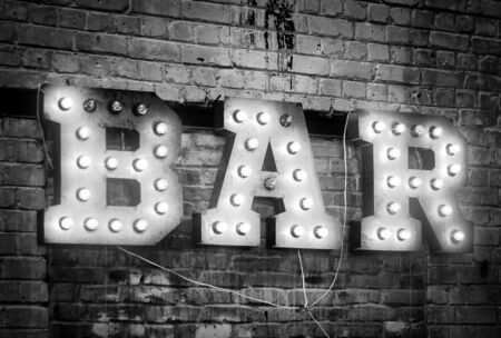 Bar signboard. Inscription from large metal letters decorated with glowing light bulbs on the brick wallの写真素材