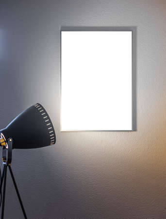 Blank vertical poster in a frame on the wall illuminated by a tripod floor lampの写真素材