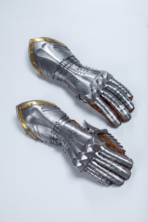 Pair of steel knight gauntlets with golden accents. Detailed metallic hand protection gloves, part of historical armor, lying side by side on a light uniform background.の写真素材