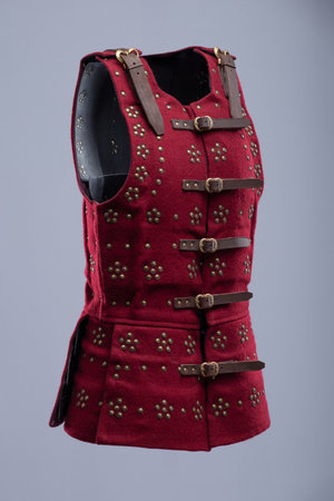 Red Medieval Brigandine with Studded Detail. Sleeveless torso armor featuring numerous studded embellishments and adjustable leather straps with brass buckles.の写真素材