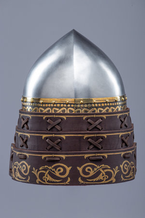 Ancient Metallic Helmet with Ornate Leather Details. Historical head protection featuring a shiny metal dome and decorated leather bands with intricate patterns.の写真素材