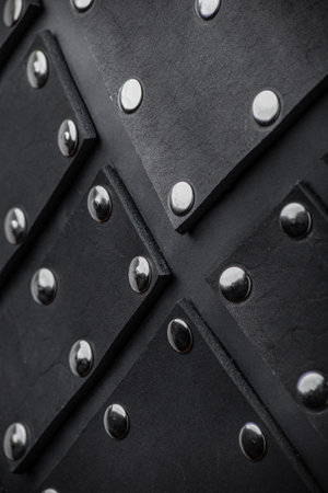 Close-Up Detail of Black Leather Armor with Metal Rivets. Detailed texture of a protective leather garment adorned with shiny metal studs.の写真素材
