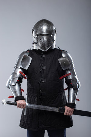 Knight in Full Plate Armor Holding a Sword. This image shows a person fully clad in shiny silver plate armor, including a helmet with a perforated visor, gauntlets, and articulated leg and arm pieces, holding a large sword with both hands.の写真素材