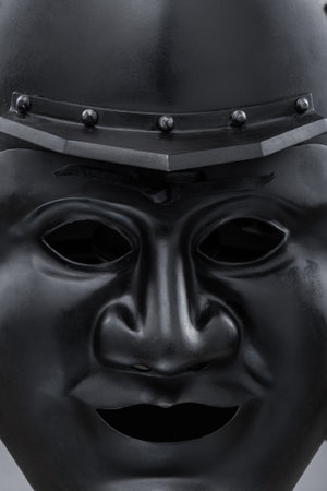 Dark Samurai Helmet with Menacing Face Mask. This image features a dark, almost black, samurai helmet with a detailed face mask displaying a fierce expression.の写真素材