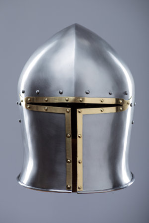 Silver Medieval Barbute Helmet with Brass Trim. This image shows a shiny silver helmet with a distinctive T-shaped opening for the face, accented with brass trim and rivets.の写真素材