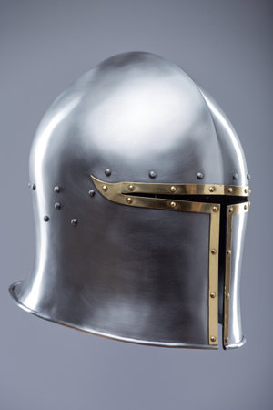 Silver Medieval Barbute Helmet with Brass Trim. This image shows a shiny silver helmet with a distinctive T-shaped opening for the face, accented with brass trim and rivets.の写真素材