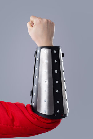 Silver Splinted Bracer on an Arm. This image shows a silver metal splinted bracer being worn on a person's forearm over a red garment. The bracer has black leather trim and is secured with rivets. The hand is clenched into a fist.の写真素材