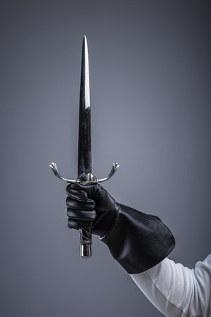 Gloved Hand Holding Sharp Medieval Dagger. Close-up of a hand in leather glove gripping a pointed...
