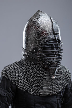Dark Helmet with Ribbed Faceplate and Chainmail. This image shows a dark, possibly blackened steel, helmet with a pointed top and a distinctive faceplate featuring a series of horizontal ribs. A chainmail collar extends from the base of the helmet.の写真素材