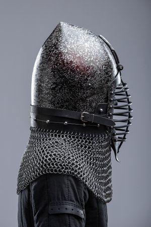 Dark Helmet with Ribbed Faceplate and Chainmail. This image shows a dark, possibly blackened steel, helmet with a pointed top and a distinctive faceplate featuring a series of horizontal ribs. A chainmail collar extends from the base of the helmet.の写真素材