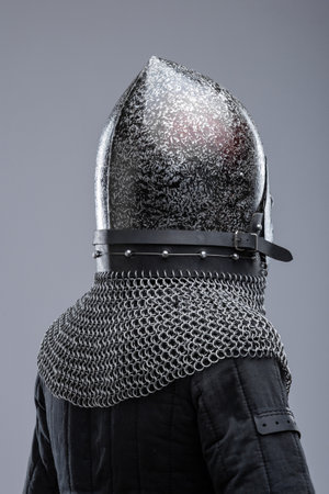 Dark Metal Helmet with Pointed Top and Faceplate. This image shows a dark metal helmet with a pointed top and a faceplate that covers the lower part of the face, featuring several horizontal slits for vision. A chainmail collar is attached to the helmet.の写真素材
