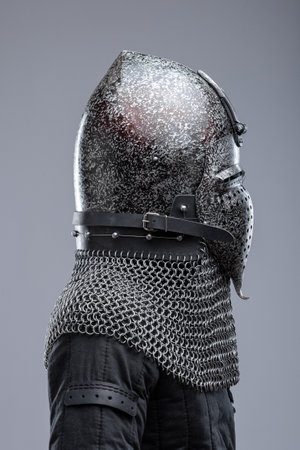 Dark Metal Helmet with Pointed Top and Faceplate. This image shows a dark metal helmet with a pointed top and a faceplate that covers the lower part of the face, featuring several horizontal slits for vision. A chainmail collar is attached to the helmet.の写真素材