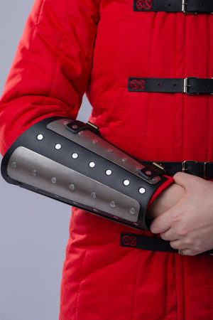 Close-Up of Silver Splinted Bracers on Red Padded Armor. This image shows a close-up of silver metal splinted bracers worn over a red padded garment, likely a gambeson. The bracers are attached with rivets and have black leather trim.の写真素材
