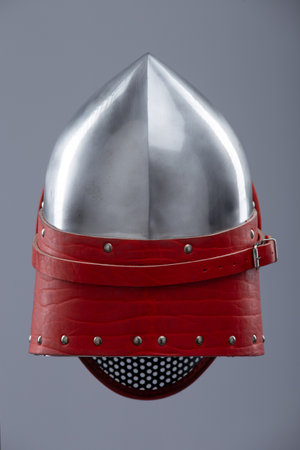 Modern fencing helmet with protective mesh visor. A shiny silver helmet features a full face mesh visor and is secured with a red leather strap and metal buckle.の写真素材
