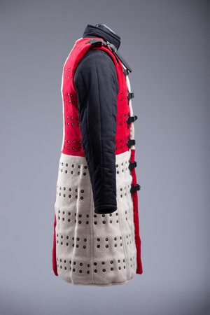 Red and White Brigandine Armor with Studs and Black Straps. This image shows a brigandine armor that is divided vertically into two halves, one red and the other white. It features rows of small brass-colored studs and is secured with multiple black leather straps and silver buckles.の写真素材