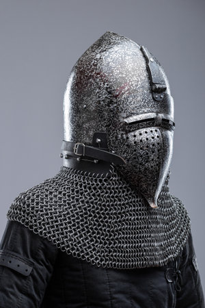 Dark Metal Helmet with Pointed Top and Faceplate. This image shows a dark metal helmet with a pointed top and a faceplate that covers the lower part of the face, featuring several horizontal slits for vision. A chainmail collar is attached to the helmet.の写真素材