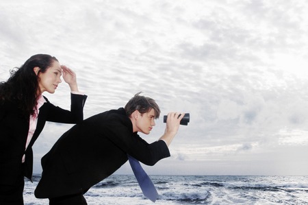 A guy using a binocular to look at the sea view whiles his girlfriend using her hand to shade...