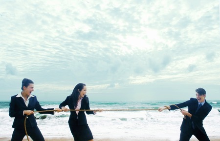 A guy playing tug of war on the beach with two ladies