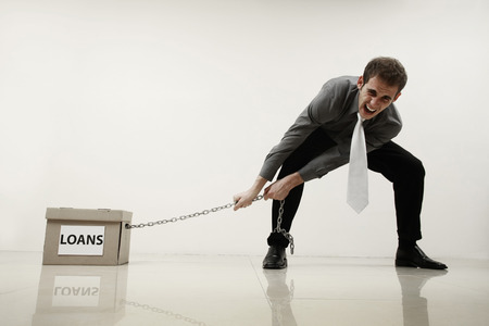 Businessman pulling a box of loans chained to his leg