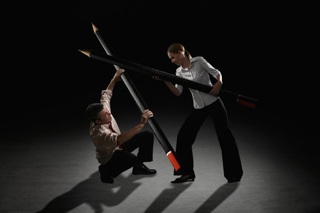 Businessman and businesswoman fighting using giant pencils