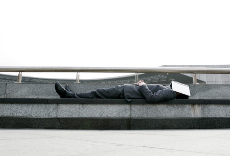 Businessman sleeping on the bench with a book covering his faceの写真素材