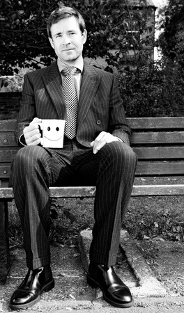 Businessman sitting on the bench holding a cup of coffeeの写真素材