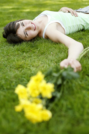 Teenage girl lying down on the field with yellow flowers in her handの写真素材