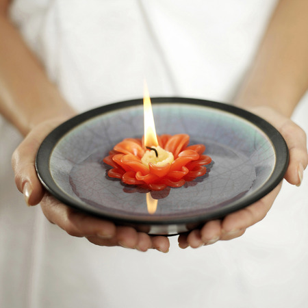 Woman holding a bowl of water with lit candle floating on itの写真素材