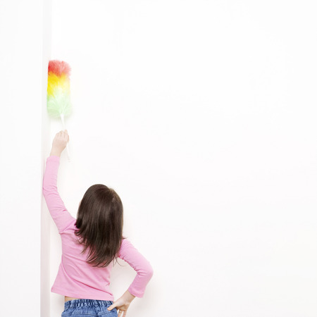 Girl dusting the wall with a feather dusterの写真素材