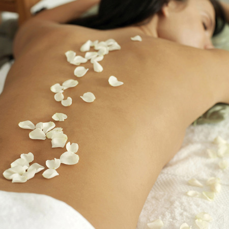 Woman lying on a massage table with rose petals on her backの写真素材