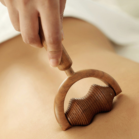 Hand using a wooden massager on woman's backの写真素材