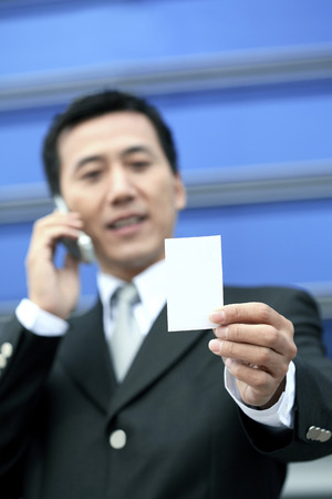 Businessman holding business card while talking on the phoneの写真素材