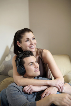 Man listening to music on the headphones with his wife beside himの写真素材