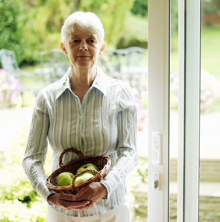 Senior lady holding a basket of fruitsの写真素材