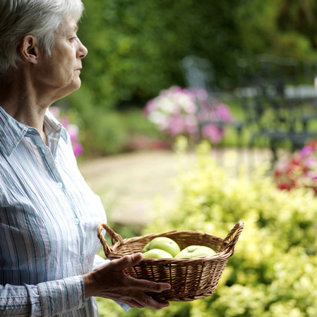 Senior lady holding a basket of fruitsの写真素材