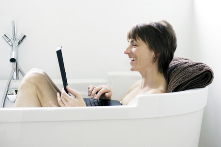 Woman sitting in the bathtub using laptop