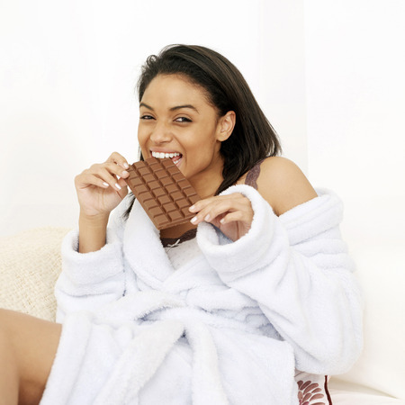 Woman in bathrobe enjoying a bar of chocolateの写真素材