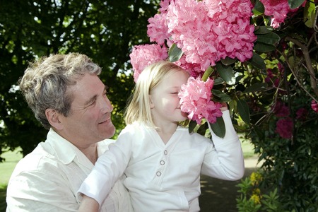 Senior man carrying girl, girl smelling flowers on plantの写真素材
