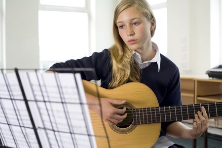 Girl plucking guitar in music room