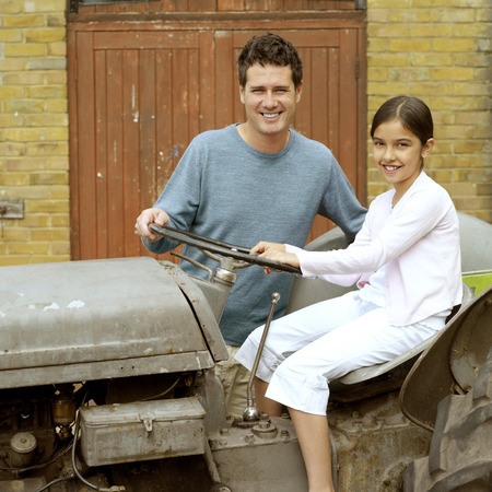 Girl sitting on a tractor with man beside herの写真素材