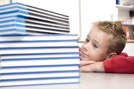 Boy looking at a stack of books beside himの写真素材