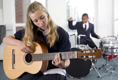Girl plucking guitar with boy playing drum in the backgroundの写真素材