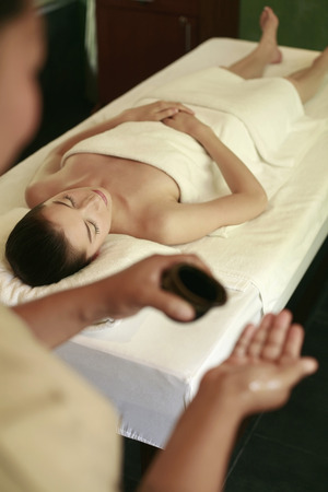 Woman lying on massage table, massage therapist pouring oil on palmの写真素材