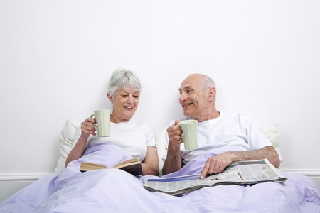 Senior man and woman drinking tea while reading in the bedroomの写真素材