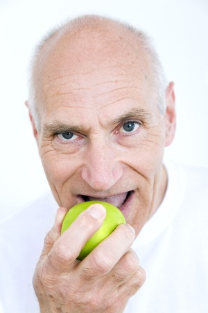 Senior man biting on a green appleの写真素材