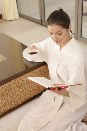 Woman holding a cup of tea while reading bookの写真素材