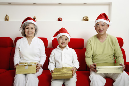 Boy sitting in between senior man and senior woman, each holding a presentの写真素材