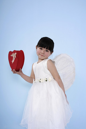 Girl wearing white dress with angel wings holding red heart-shaped boxの写真素材