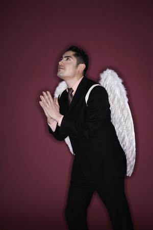 Businessman with angel wings praying while looking upの写真素材